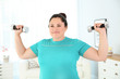 © New Africa - Overweight woman doing exercise with dumbbells at home