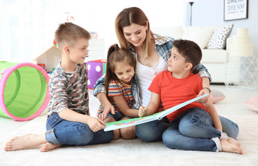 Canvas Print - Cute little children reading book on floor with young mother in playing room