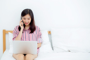 Wall Mural - Portrait asian young woman on bed using laptop computer and talk smart phone at bedroom for leisure and relax, freelance with girl working notebook and calling telephone, communication concept.