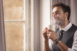 © Teodor Lazarev - Handsome business man enjoying his morning cup of coffee, getting ready for work, enjoying city view from a window