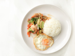 Fried Savory sauteed mixed vegetables with shimp and fried egg served with rice in white dish on white background as Thai homemade meal or recipe in the restaurant. Thai style food.