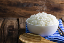 Cooked Rice In A White Bowl With Smoke On Wooden Floor