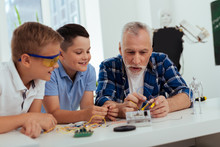 Smart Grandfather. Positive Joyful Man Talking To His Grandchildren While Explaining To Them How To Build A Robot