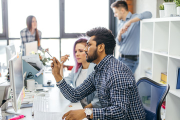 Young Indian constructor sharing new ideas about project to his partners in office working room. Multiethnic coworkers discussing over new business project in modern loft interior.