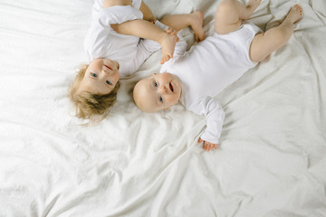 Two charming little babies lie on the white sheet and smile