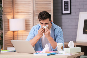 Poster - Sad exhausted man with tissue suffering from cold while working with laptop at table