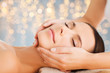 © Syda Productions - wellness, spa and beauty concept - close up of beautiful woman having face massage over holidays lights background