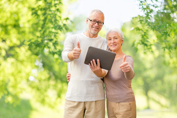 Canvas Print - technology and people concept - senior couple with tablet pc computer showing thumbs up over green natural background