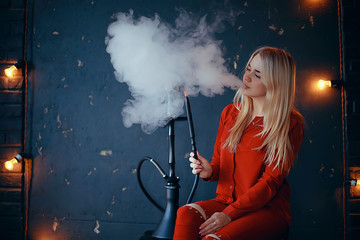 girl smokes  hookah / beautiful glamorous girl in red dress smokes a hookah, the sexy model in a night club smokes