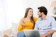 © W PRODUCTION - cheerful young couple on sofa at home websurfing and shopping online with laptop computer internet technology