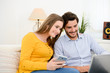 © W PRODUCTION - cheerful young couple on sofa at home websurfing and shopping online with laptop computer internet technology