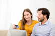 © W PRODUCTION - cheerful young couple on sofa at home websurfing and shopping online with credit card, a laptop computer and internet technology