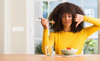 Canvas Print - African american woman eating pasta salad at home with angry face, negative sign showing dislike with thumbs down, rejection concept