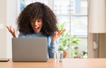 Wall Mural - African american woman using laptop computer at home very happy and excited, winner expression celebrating victory screaming with big smile and raised hands