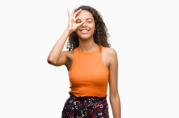 Wall Mural - Young hispanic woman with happy face smiling doing ok sign with hand on eye looking through fingers