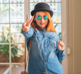 Sticker - Stylish redhead woman wearing bowler hat and sunglasses smiling looking to the camera showing fingers doing victory sign. Number two.