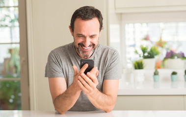 Middle age man using smartphone with a happy face standing and smiling with a confident smile showing teeth