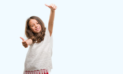 Brunette hispanic girl approving doing positive gesture with hand, thumbs up smiling and happy for success. Looking at the camera, winner gesture.