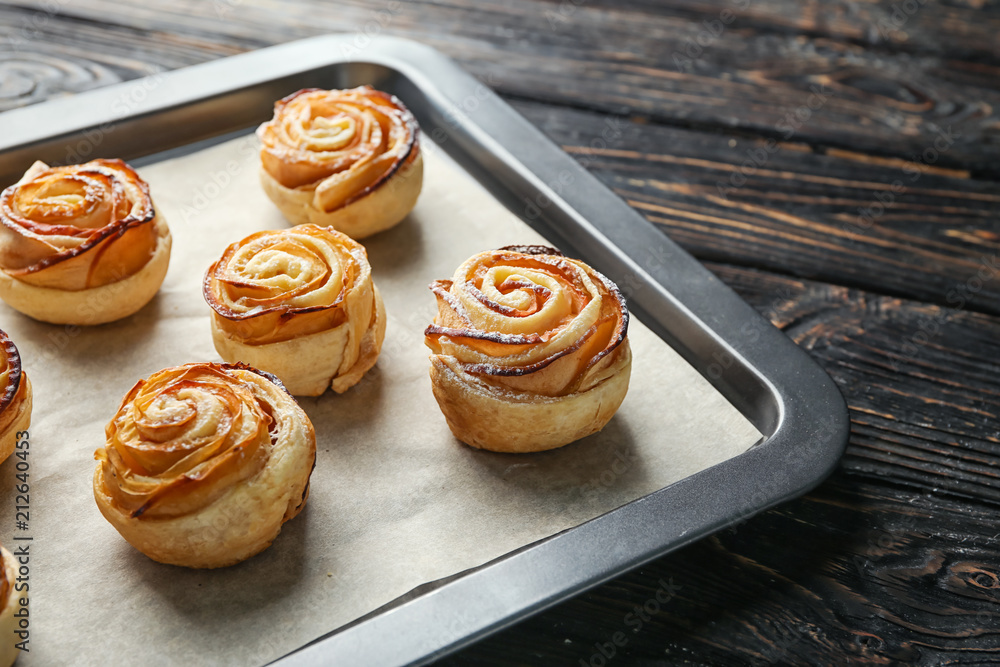 Baking tray with apple roses from puff pastry on wooden background, closeup