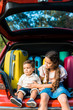© LIGHTFIELD STUDIOS - brother and sister sitting near travel bags in car trunk