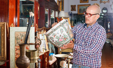 Portrait Of Mature Man Choosing Vintage Goods At Antiques Shop