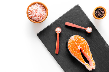 Make salty fish. Raw salmon steak on cutting board near bowl with salt and pepper on white background top view copy space