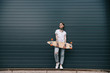 © LIGHTFIELD STUDIOS - distant view of young woman with tattoos holding skateboard against black wall