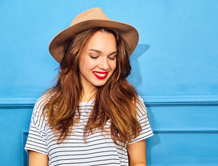 Young stylish girl model in casual summer clothes  and brown hat with red lips, posing near blue wall