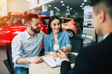 Wall Mural - Husband bought his wife the first car. Happy married couple gets the keys from the seller in the dealership.