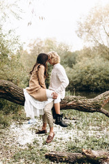 A beautiful couple in the boo style embraces sitting on a branch over the lake