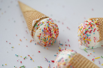 Waffle cone with white ice cream and sweet sprinkles on a light background