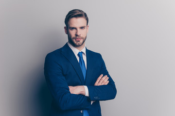 Wall Mural - Portrait with copy space of cool, brutal, stunning, brunet, serious, concentrated man with stubble in blue suit with tie, having his arms crossed, looking at camera, isolated on grey background