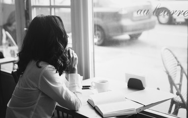 Woman sits in a cafe with a cup of coffee, tea. Read a book and dream. Look  out the window. Wait for somebody.