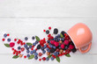 © MK studio - Various fresh berries close-up including blueberries, raspberries, blackberries currants and gooseberries drop out of a cup on a white wooden background. Top view