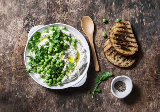 Fresh ricotta cheese with green peas, olive oil, pepper and herbs on a wooden background, top view. Healthy diet food - delicious breakfast, snack