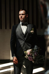 A man in a classic suit by the window.A man with a bouquet.Morning bridegroom.