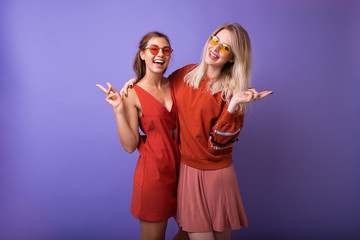 Studio lifestyle portrait of two best friends hipster girls wearing stylish bright orange outfits, dresses and sweater,sunglasses.Two beautiful young women in casual clothes in studio.