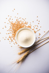 Raw unprepared semolina flour also known as Rava powder in Hindi in bowl or spoon. close-up isolated on white or moody background. selective focus