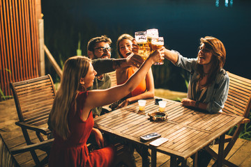 Group of friends drink beer on the terrace and toast during summer night