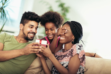 Happy black family at home. African american father, mother and child celebrating birthday, having fun at party.Daughter giving gift to mother