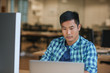 © mavoimages - Focused young Asian designer using a laptop at his desk