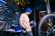 © Elizaveta - A young, stylish redheaded male small business owner selling and repairing a bike is wearing a blue cap and a pink jersey is using a mobile phone while standing in a bike shop.