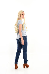 Poster - full length portrait of blonde girl wearing casual blue shirt and jeans, standing pose with back to the camera. isolated on white studio background.