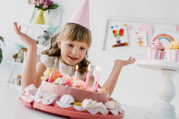 smiling little child with wide arms looking at birthday cake with candles