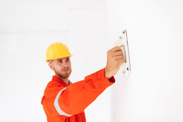 Wall Mural - Close up foreman in orange work clothes and yellow hardhat using putty knife at work isolated