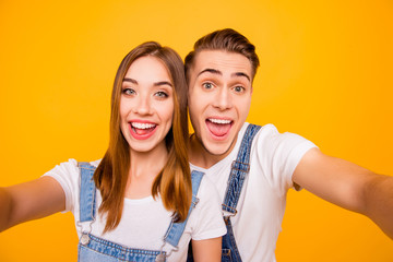 Self portrait of beautiful cheerful funny foolish adorable young cute couple smiling, looking straight with opened mouths over yellow background, isolated