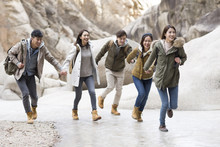 Happy Young Chinese Friends Holding Hands Running Outdoors In Winter 
