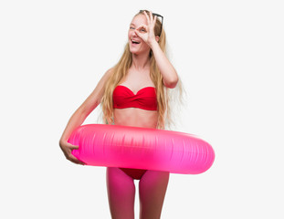 Sticker - Blonde teenager woman wearing bikini and holding pink floater with happy face smiling doing ok sign with hand on eye looking through fingers