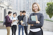 © Blue Jean Images - Cheerful female abroad student on campus with her friends in background