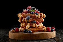 freshly baked stack of belgian waffles with berries on wooden cutting board on black